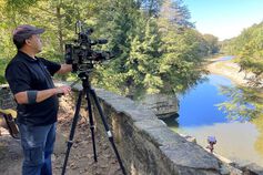 A male student uses a professional camera to film an outdoor scene.